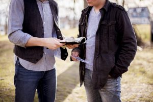 A closeup shot of two males standing near each other and reading the bible with a blurred background